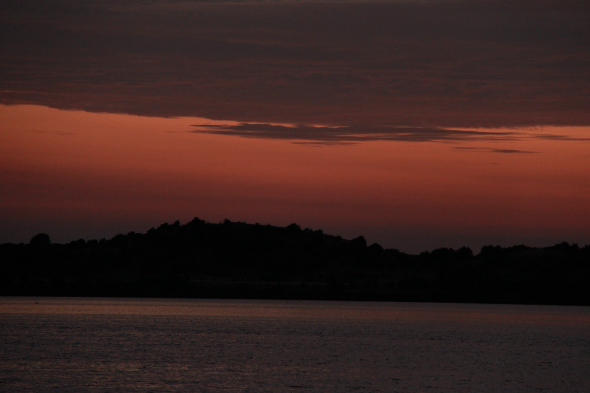 Sunset over water and silhouetted landscape